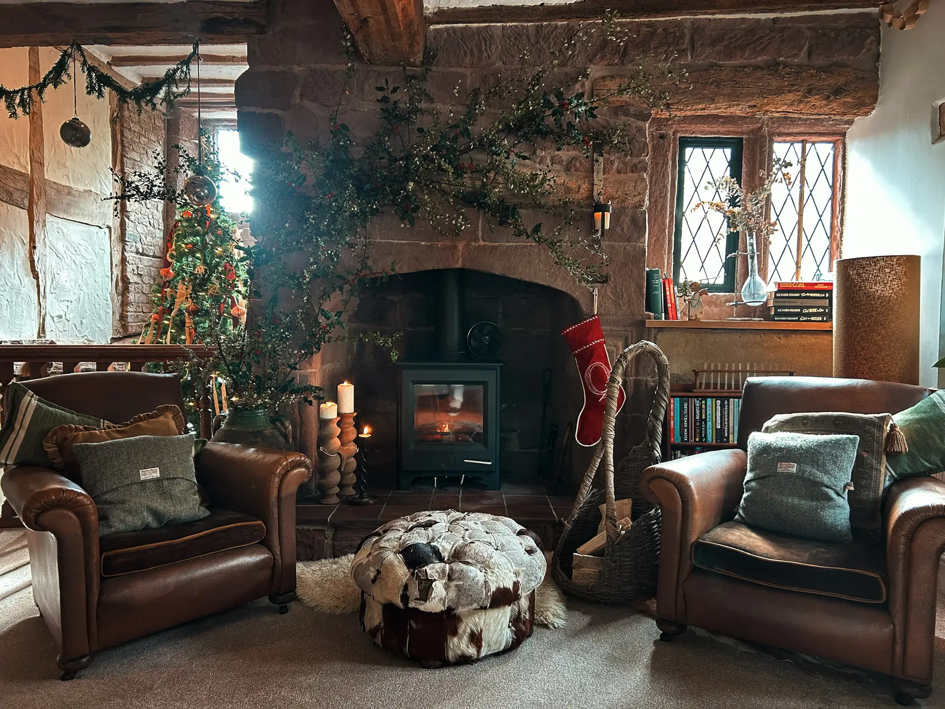 Two leather armchairs by the wood burner in the manor's stone inglenook, dressed with holly and a Christmas tree